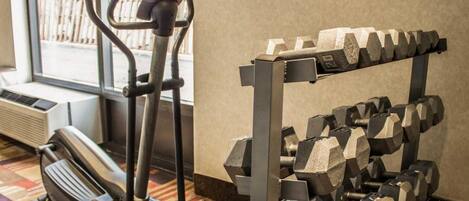 A gym with a stationary bike, elliptical, and a rack of dumbbells.