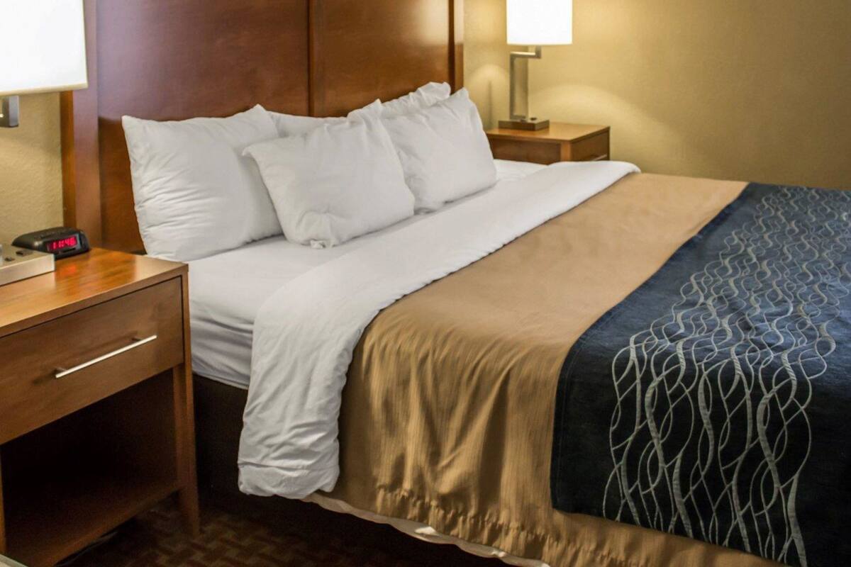 A hotel room with a bed, two bedside tables, a nightstand, a lamp, and a clock.