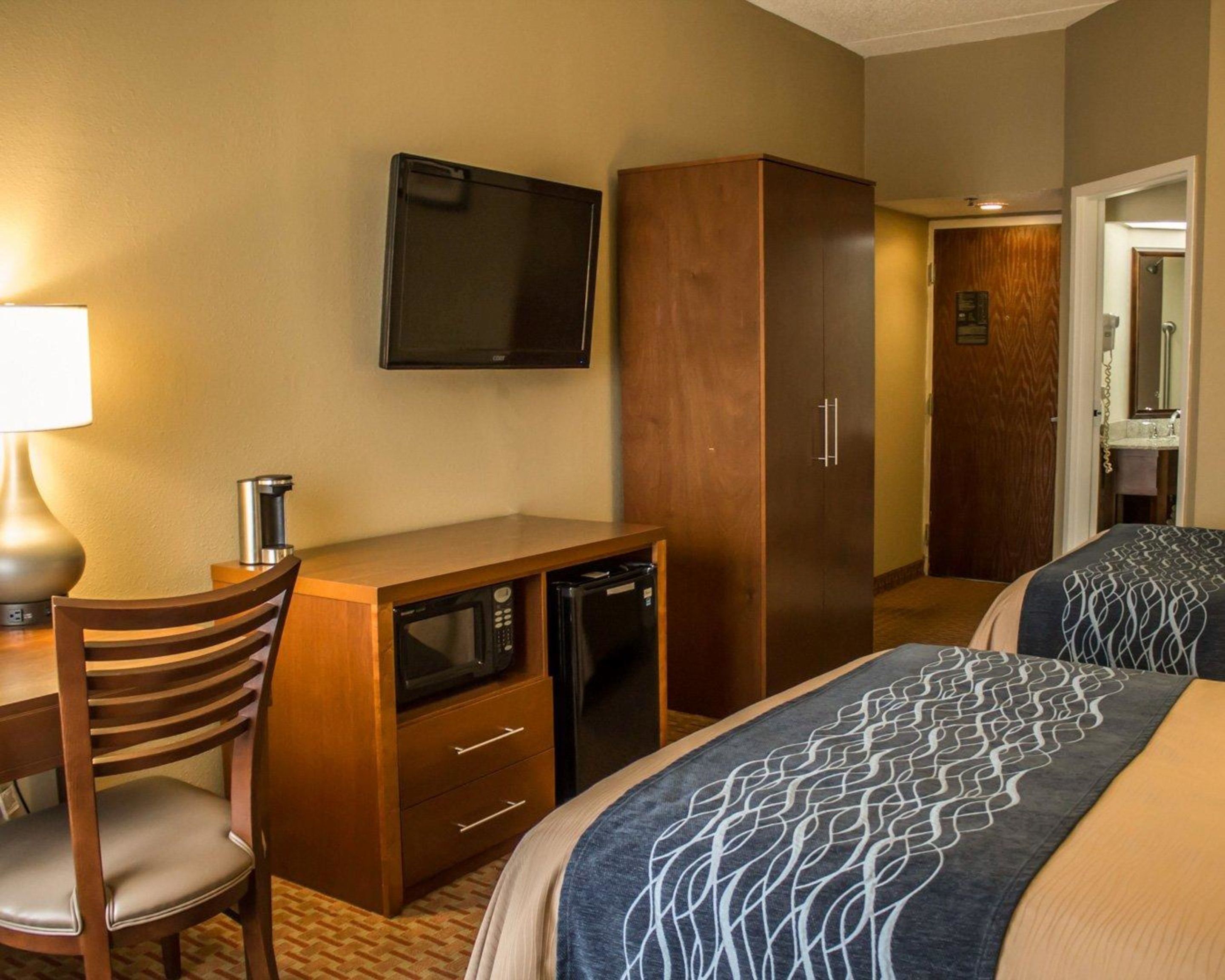 A hotel room with a desk, microwave, refrigerator, television, wardrobe, and two beds.