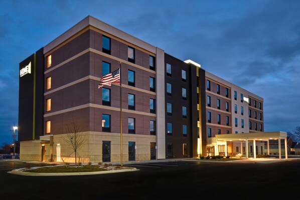 A multi-story hotel with a prominent American flag, a covered entrance, and a parking lot. - Home2 Suites by Hilton Bowling Green (Bowling Green)