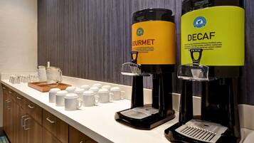 Una estació de cafè amb dos dispensadors de cafè indicats com 'GOURMET' i 'DECAF', un safata amb tasses de cafè i un molinera de cafè.