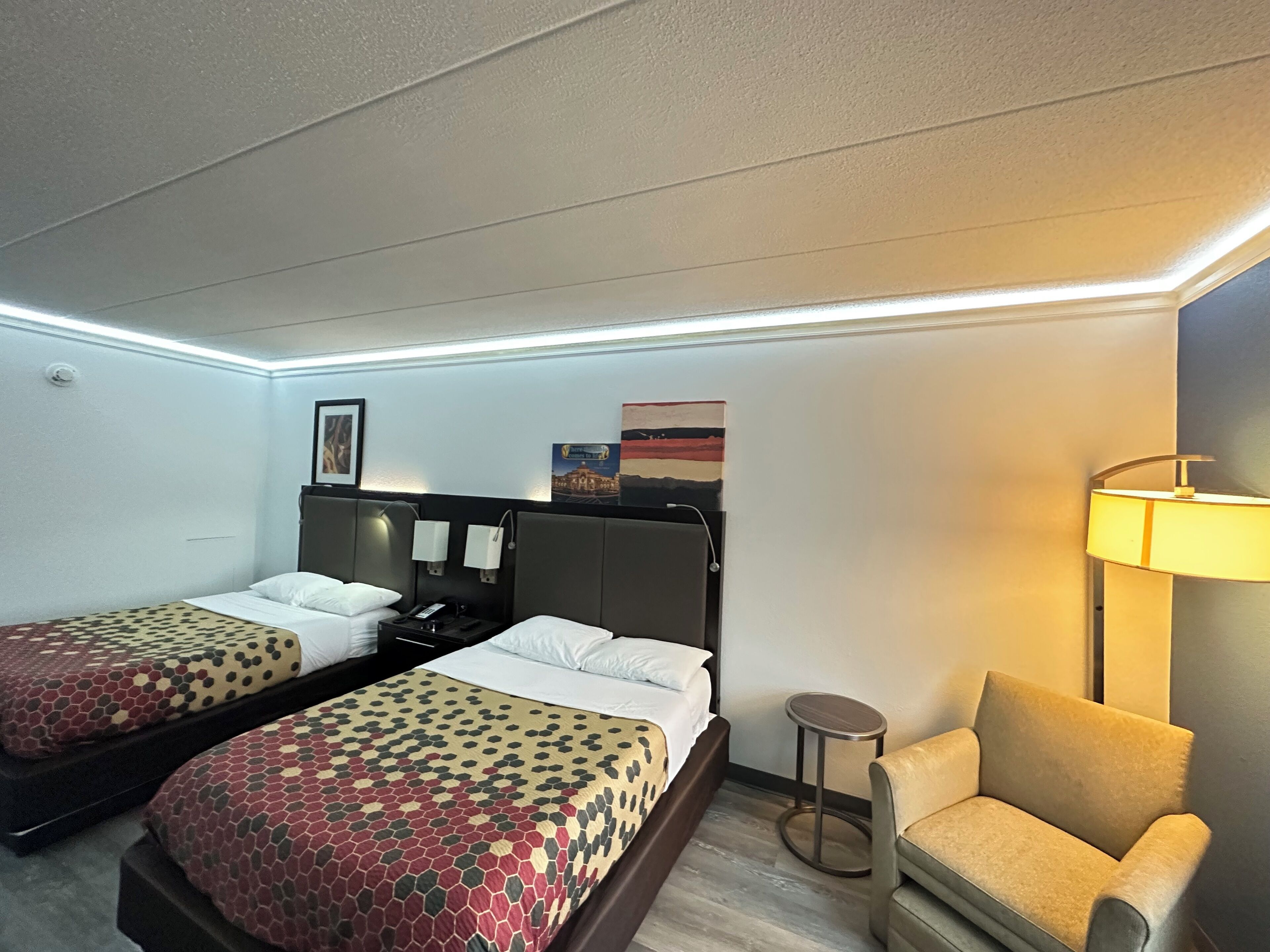 A hotel room with two beds, a sofa, a lamp, and artwork on the wall.
