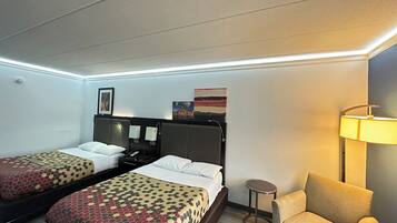 A hotel room with two beds, a sofa, a lamp, and artwork on the wall.