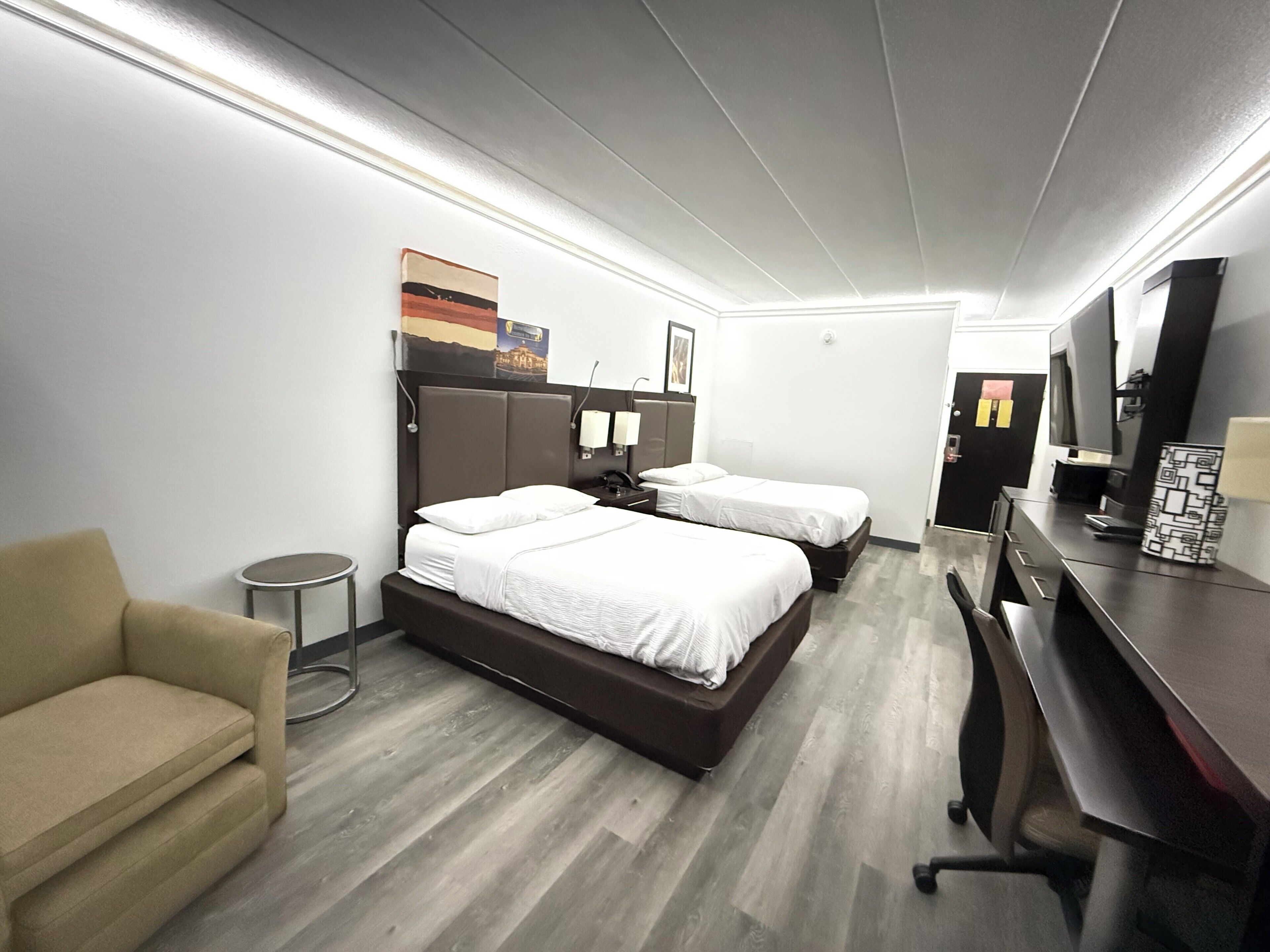 A hotel room with two beds, a desk, a chair, and a small round table.