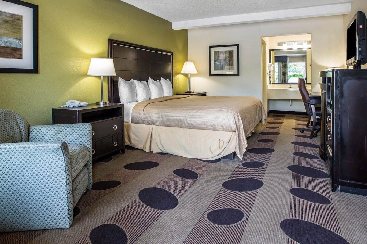 A hotel room with a bed, two bedside tables, a desk, a chair, a television, and a mirror.