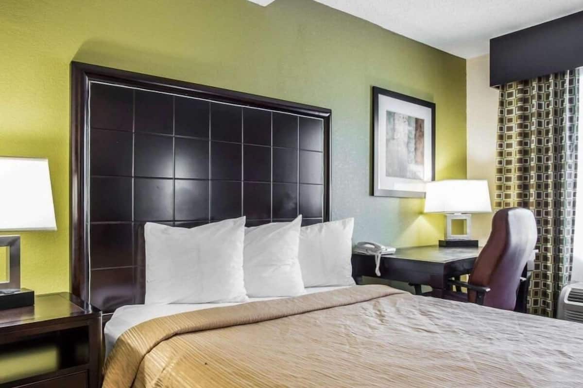 A hotel room with a large bed, a desk with a telephone, and a chair.