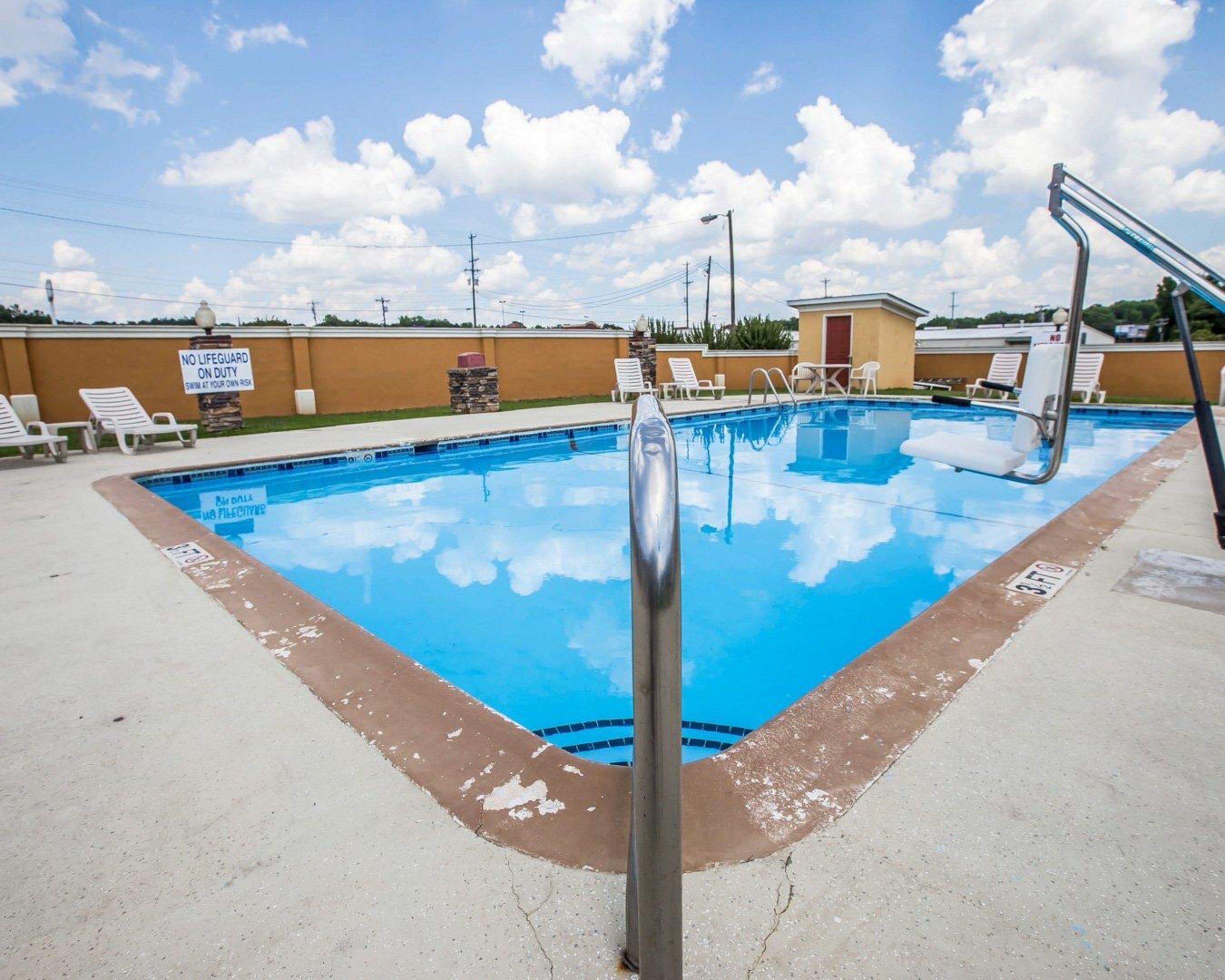A swimming pool with a lifeguard sign, lounge chairs, and a small building in the background.