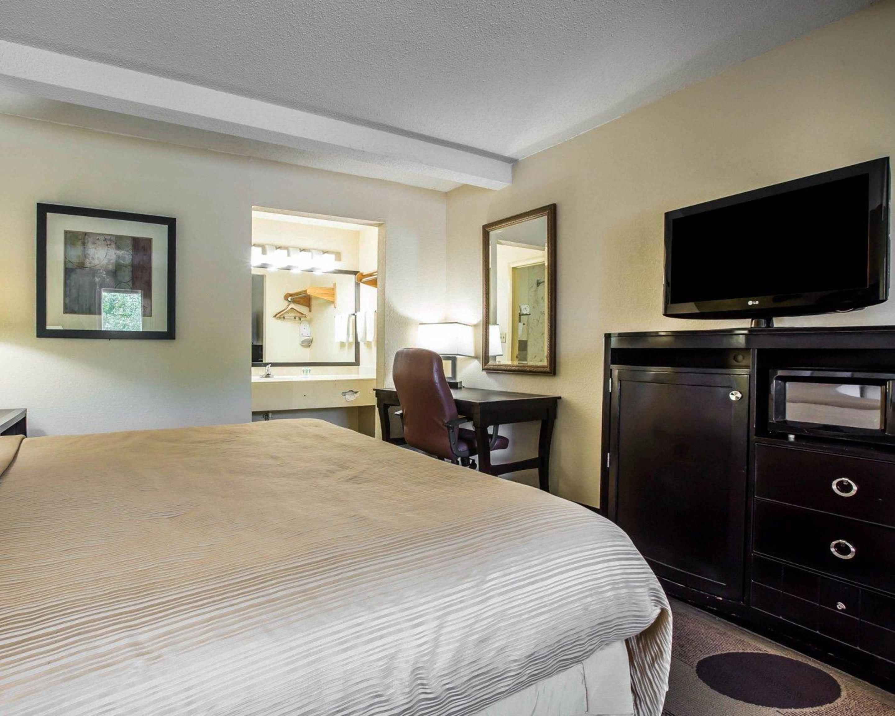 A hotel room with a bed, a desk, a chair, a TV, and a dresser.