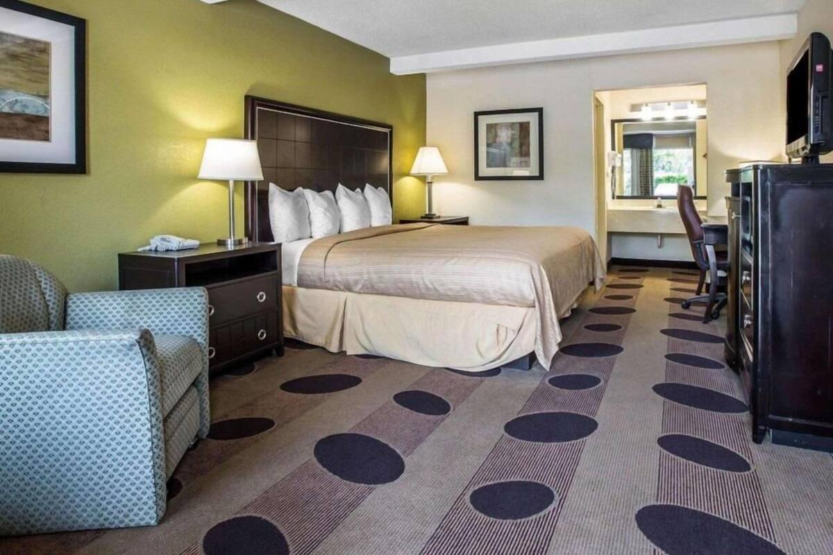 A hotel room with a bed, bedside tables, a desk, a chair, a television, and a bathroom visible through an open door.