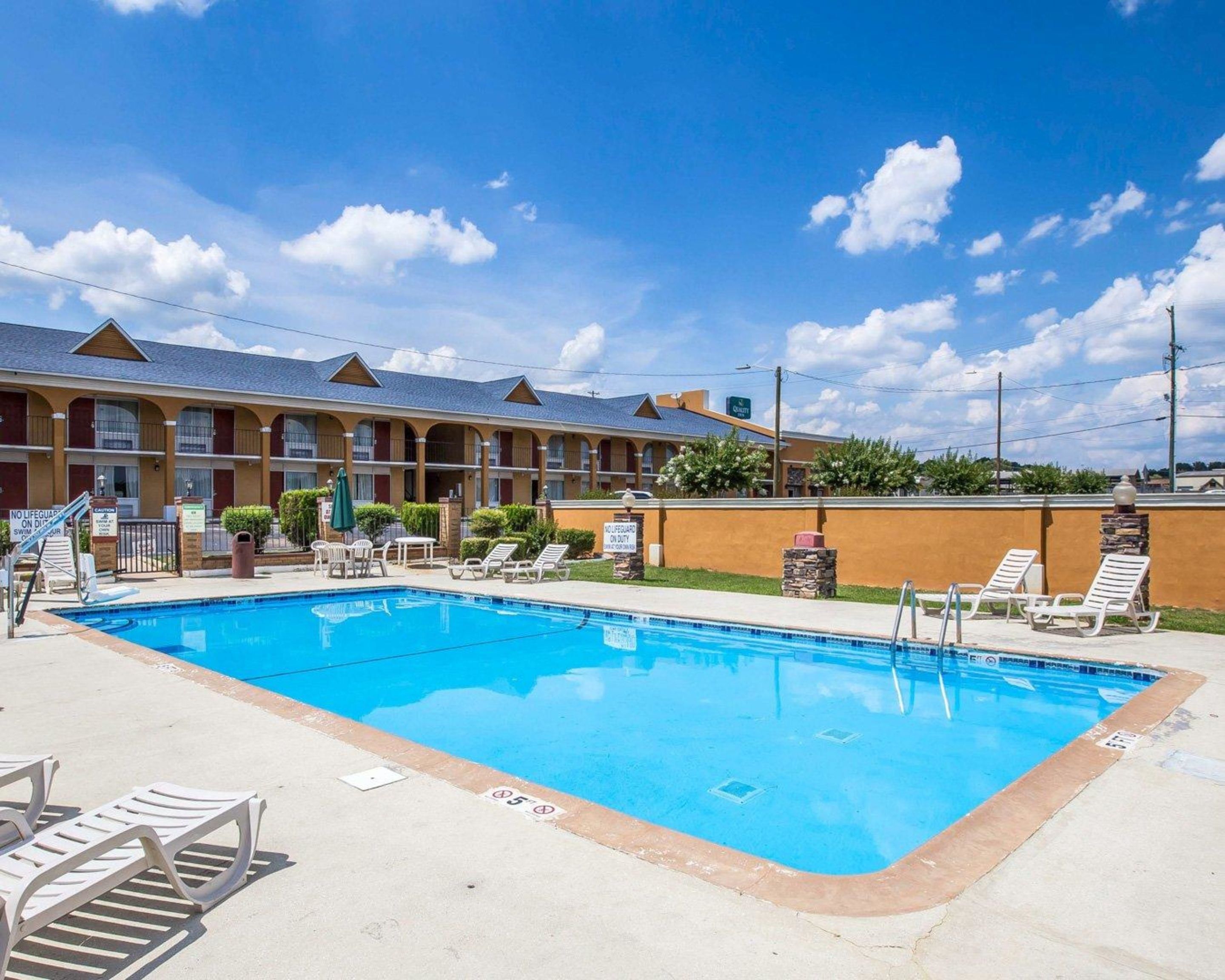 A hotel with a swimming pool, lounge chairs, and a no lifeguard on duty sign.