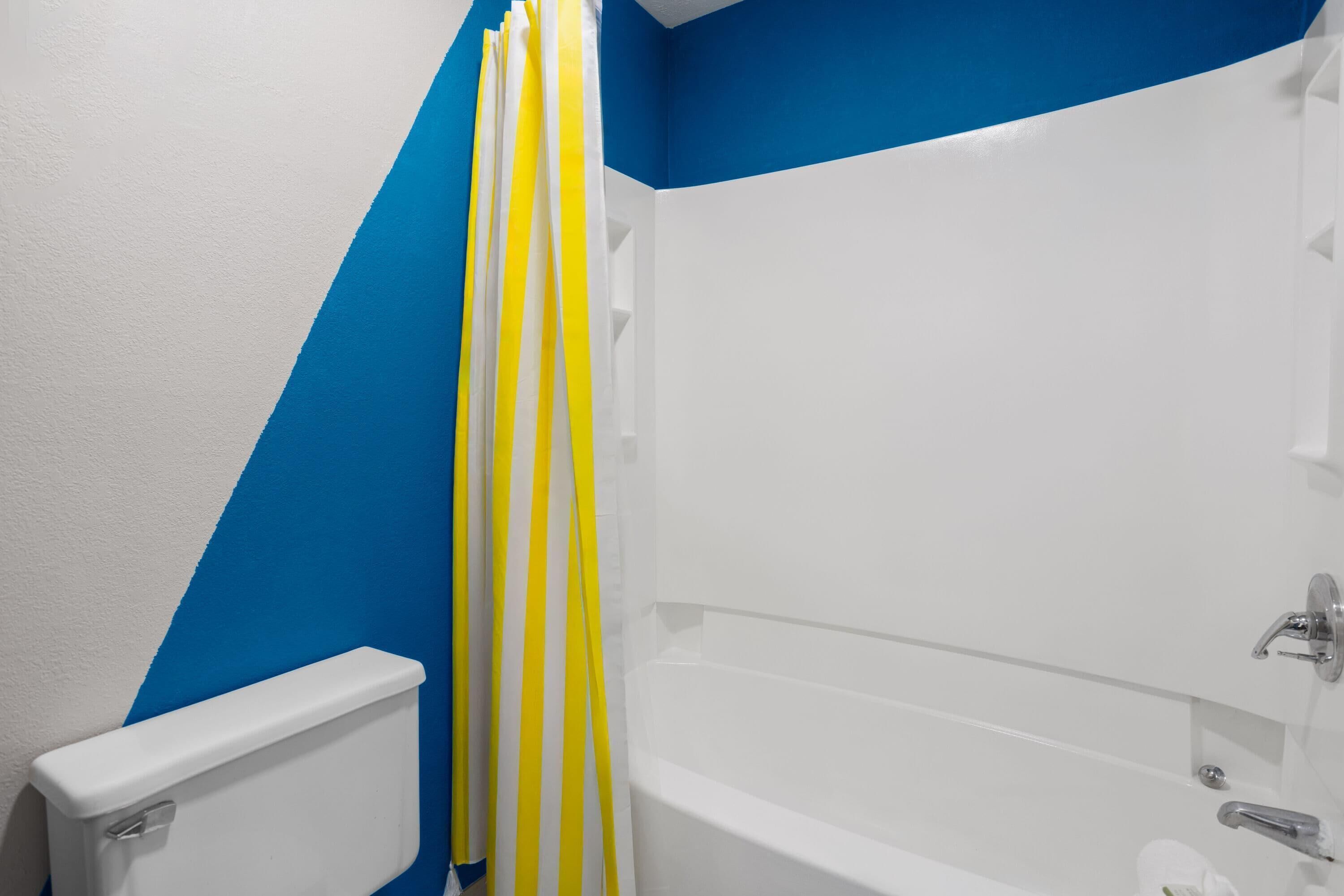 A bathroom with a white bathtub, a toilet, and a shower curtain with yellow and white stripes.