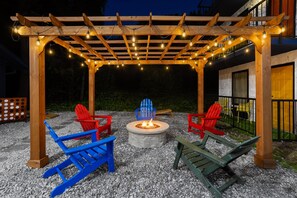 An outdoor seating area with a fire pit, wooden chairs, and a pergola with string lights. - Days Inn By Wyndham Pigeon Forge South (Pigeon Forge)
