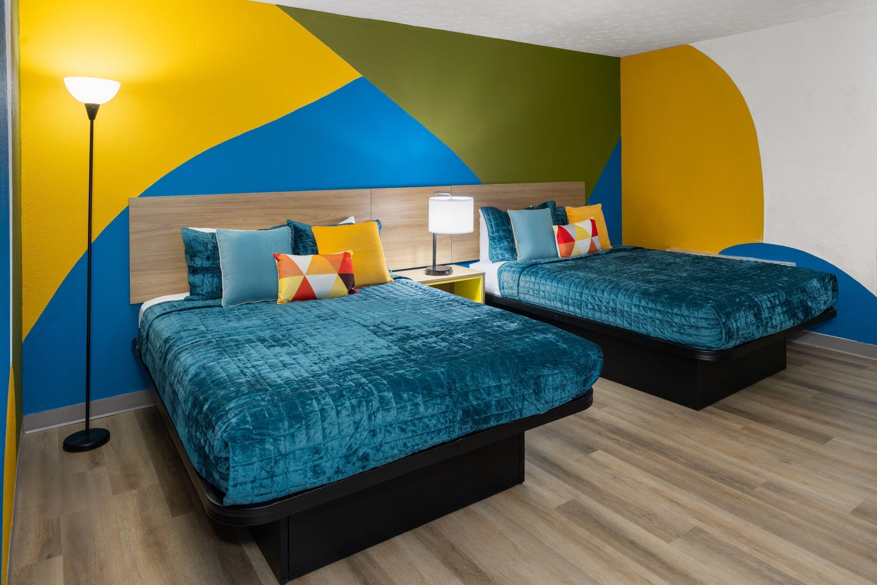 A hotel room with two beds, a nightstand, a lamp, and a wall with a geometric design.