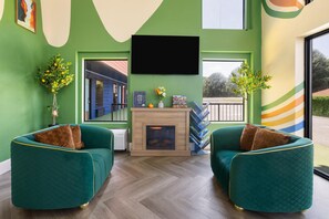 Une pièce avec deux fauteuils de couleur turquoise, une cheminée, un téléviseur à écran plat et une vue sur l’extérieur.