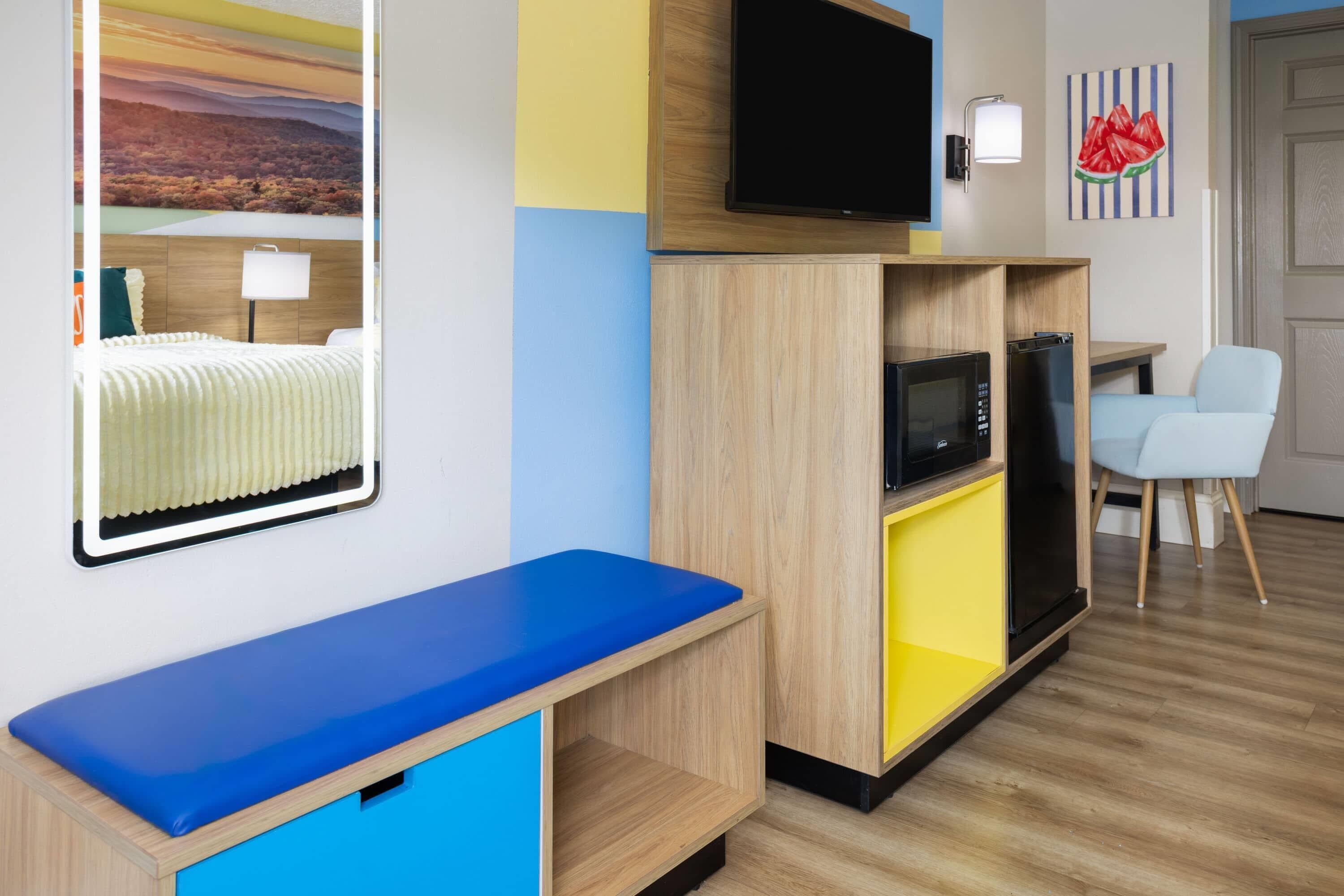 A modern hotel room with a blue sofa, a flat-screen TV, a microwave, and a refrigerator.