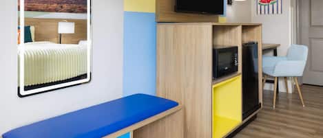 Habitación de hotel moderna con sofá azul, televisor de pantalla plana, microondas y refrigerador.