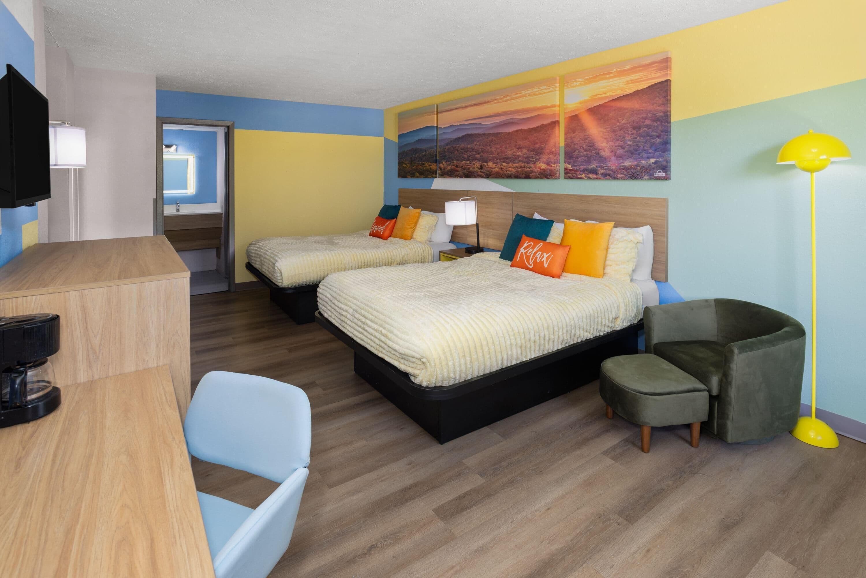 A hotel room with two beds, a desk, a chair, a sofa, a lamp, and a painting on the wall.