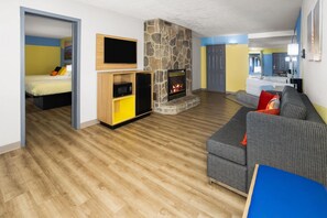 Un salon moderne avec une cheminée en pierre, un canapé, un téléviseur et un coin cuisine à l’arrière-plan.