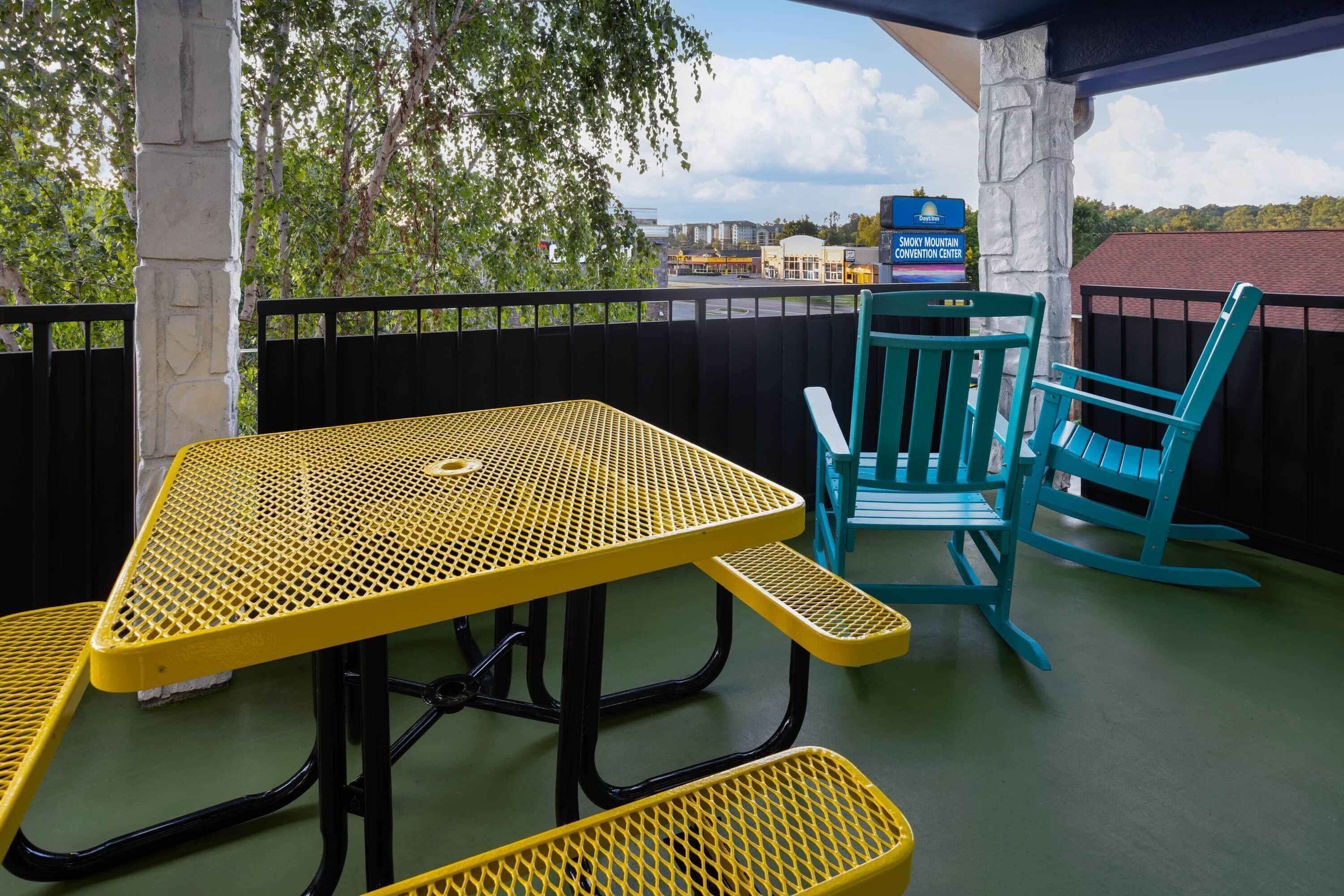 An outdoor patio with a yellow table and chairs, a stone pillar, and a view of the Smoky Mountain Convention Center in the background.