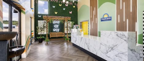 Un área de recepción con mostrador de mármol, pared verde con logotipo de Days Inn, techo a cuadros y un cartel que dice 'Good Vibe Only'.