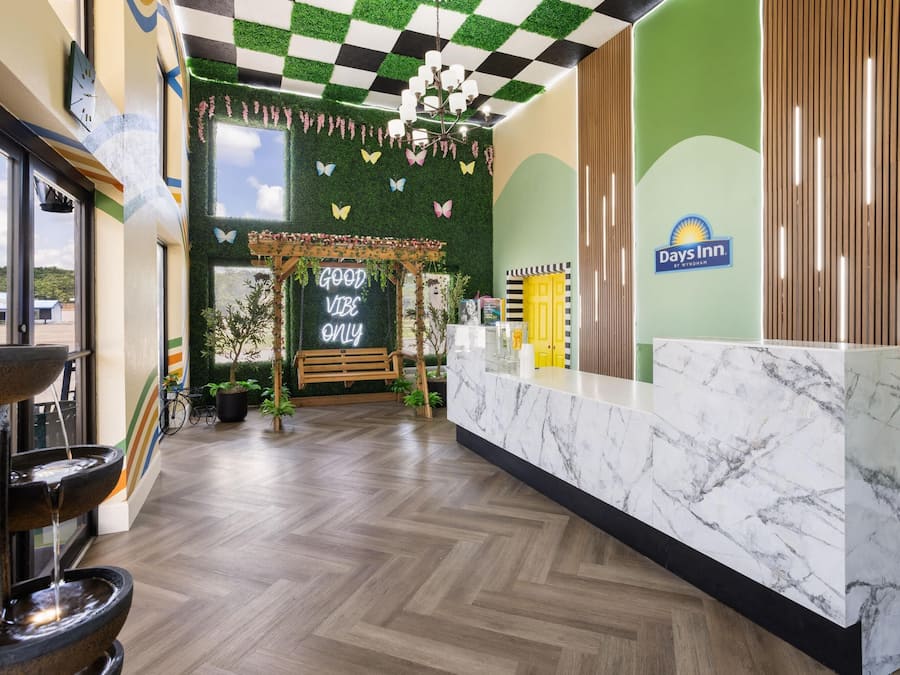 A reception area with a marble counter, a green wall with a Days Inn logo, a checkered ceiling, and a 'Good Vibe Only' sign.