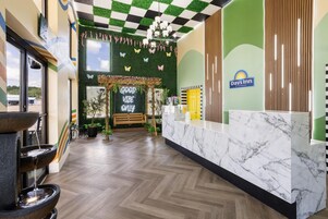 A reception area with a marble counter, a green wall with a Days Inn logo, a checkered ceiling, and a 'Good Vibe Only' sign.
