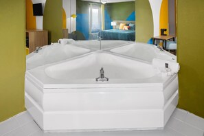 A large, white, freestanding bathtub in a room with green walls and a blue and yellow patterned wall.