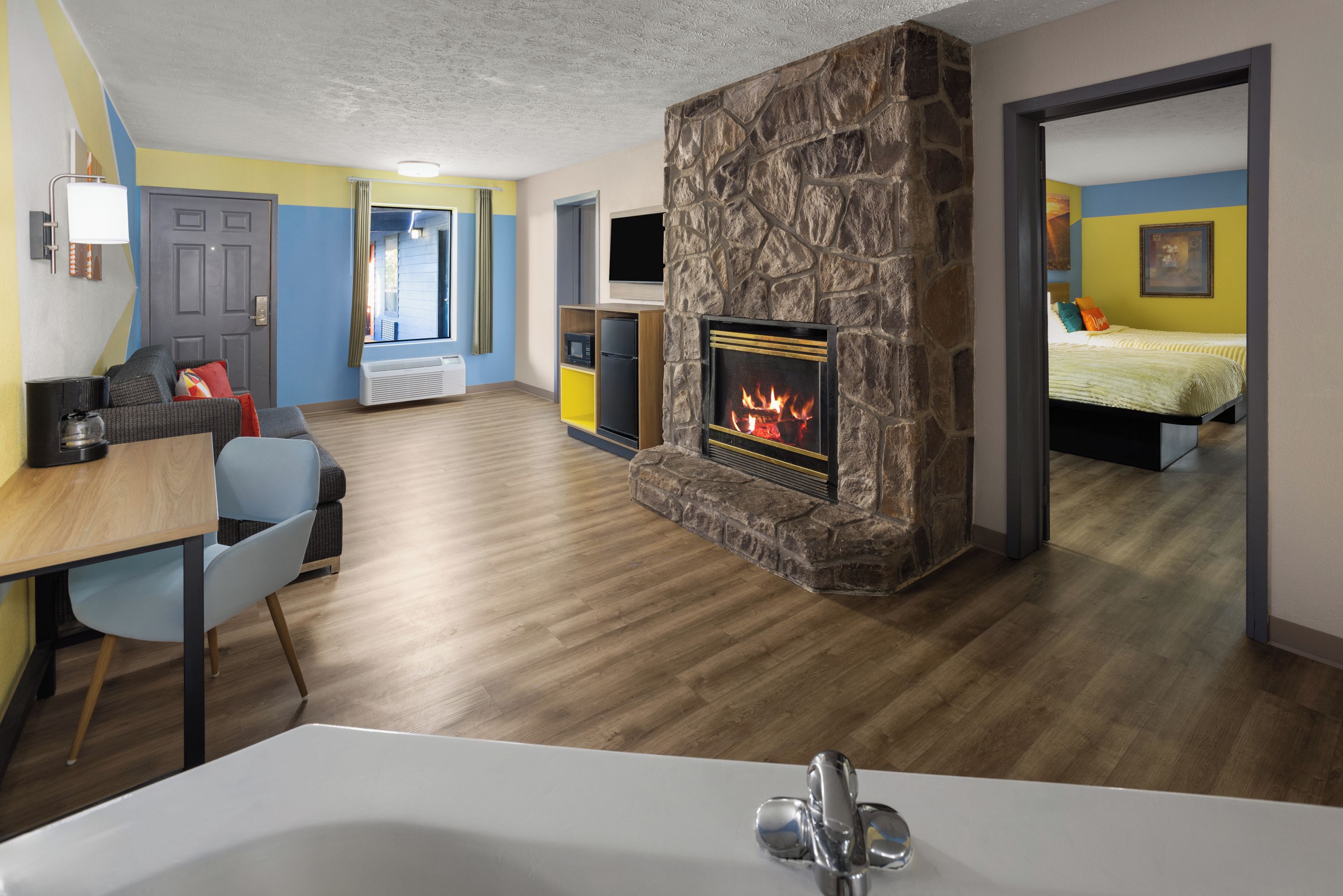 A modern living room with a fireplace, a dining area, and a bedroom visible through an open door.
