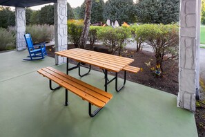 An outdoor patio with a wooden table and benches, surrounded by stone pillars and greenery. - Days Inn By Wyndham Pigeon Forge South (Pigeon Forge)
