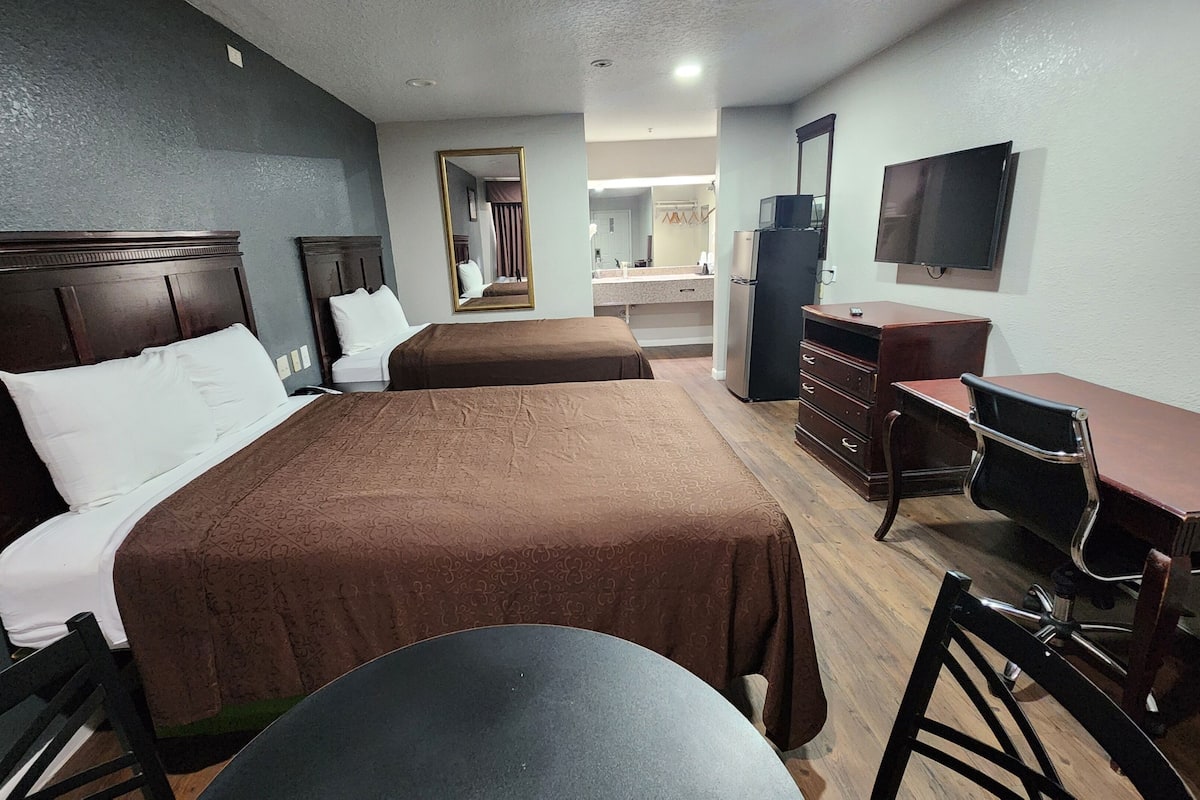 A hotel room with two single beds, a desk with a chair, a dresser, a television, and a mirror.