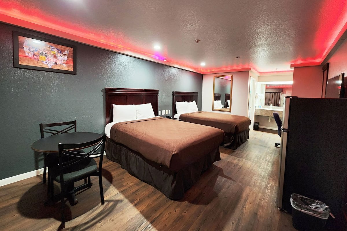A hotel room with two beds, a desk, a chair, a mirror, and a refrigerator.