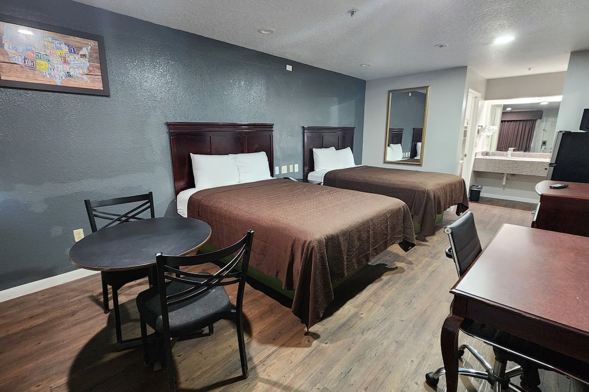 A hotel room with two beds, a desk, a chair, and a television.