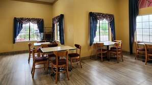 A dining area with tables and chairs, large windows with curtains, and a ceiling with a skylight. - Express Inn Hobby (Houston)