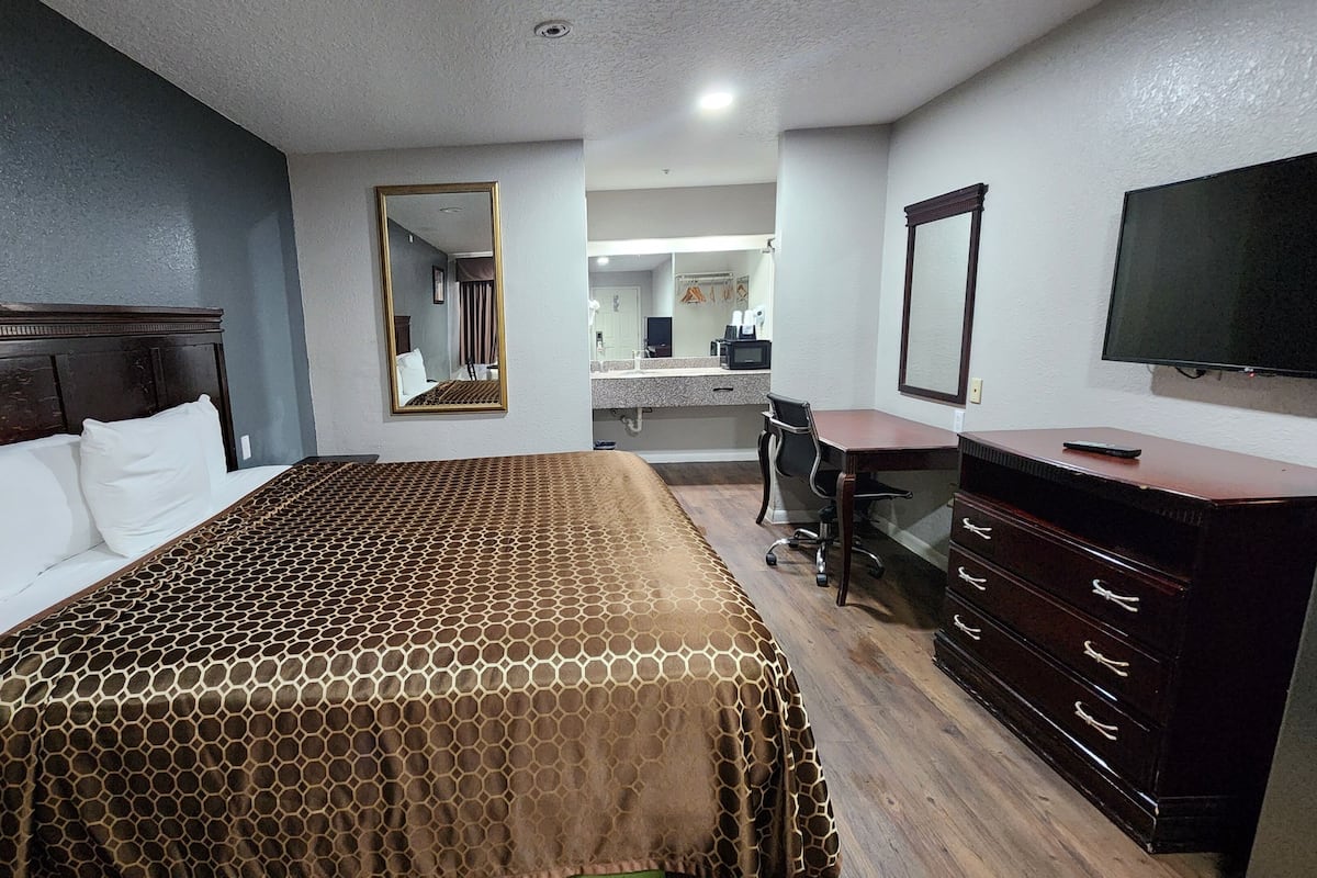 A hotel room with a large bed, a desk, a dresser, and a TV.