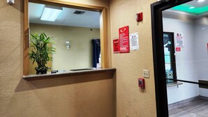 A hallway with a mirror, a potted plant, and several signs including a fire alarm and a no-smoking sign. - Express Inn Hobby (Houston)