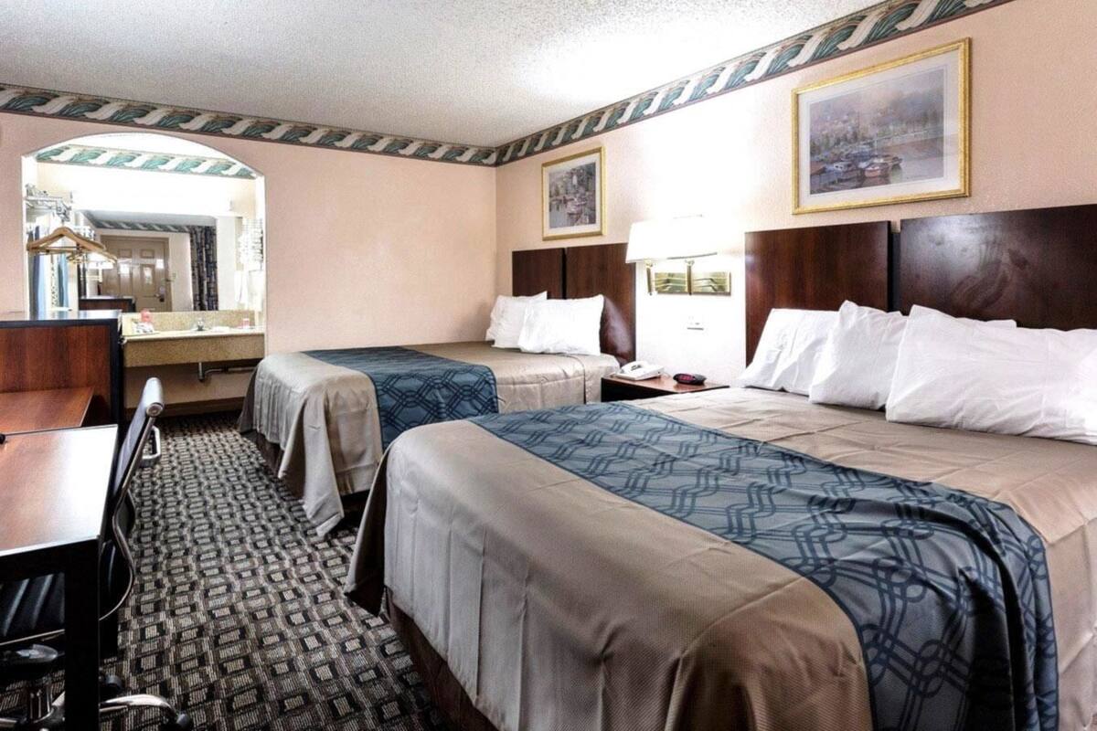A hotel room with two beds, a desk, a chair, a mirror, and a window.