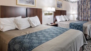 Una habitación de hotel con dos camas, cada una con cabecera, mesita de noche y lámpara. Hay cuadros enmarcados en la pared sobre las camas.