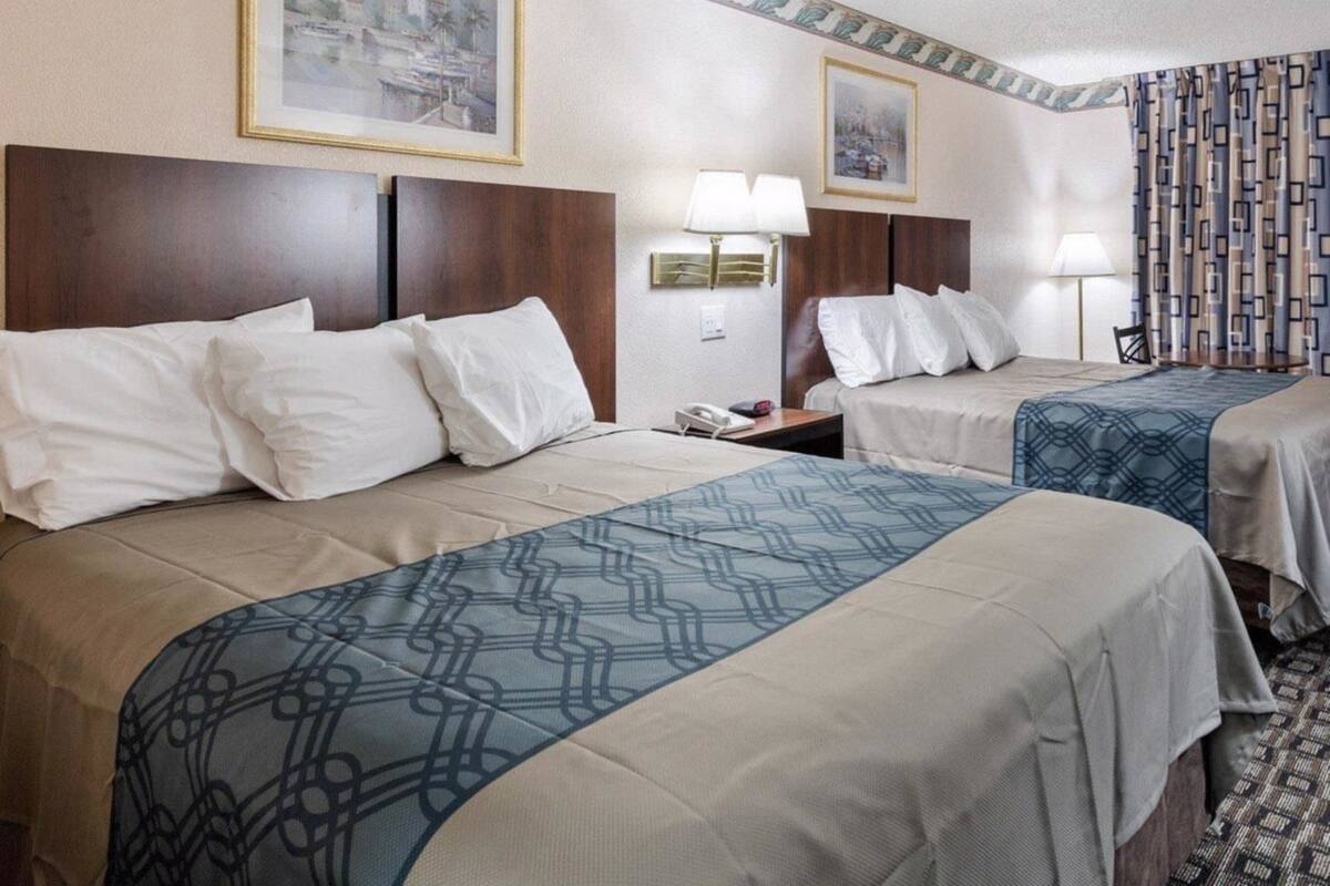A hotel room with two beds, each with a headboard, a bedside table, and a lamp. There are framed pictures on the wall above the beds.
