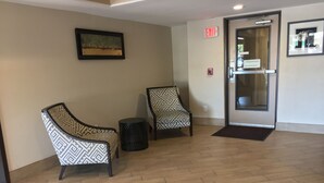 Un vestíbulo con dos sillones estampados, una mesita redonda y una puerta de salida.