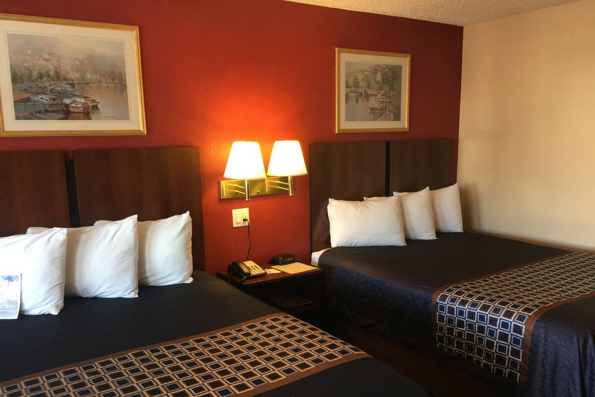 A hotel room with two beds, a nightstand with a phone, and wall-mounted lamps.
