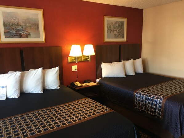 A hotel room with two beds, a nightstand with a phone, and wall-mounted lamps.