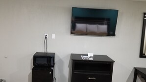 Ein Zimmer mit einem flachbildfernseher an der Wand, einem kleinen schwarzen Kühlschrank und einem schwarzen Schrank mit einer Schublade.