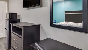 Ein Schlafzimmer mit Bett, Wand-Fernseher, Schreibtisch mit Schubladen und einem kleinen Schrank.