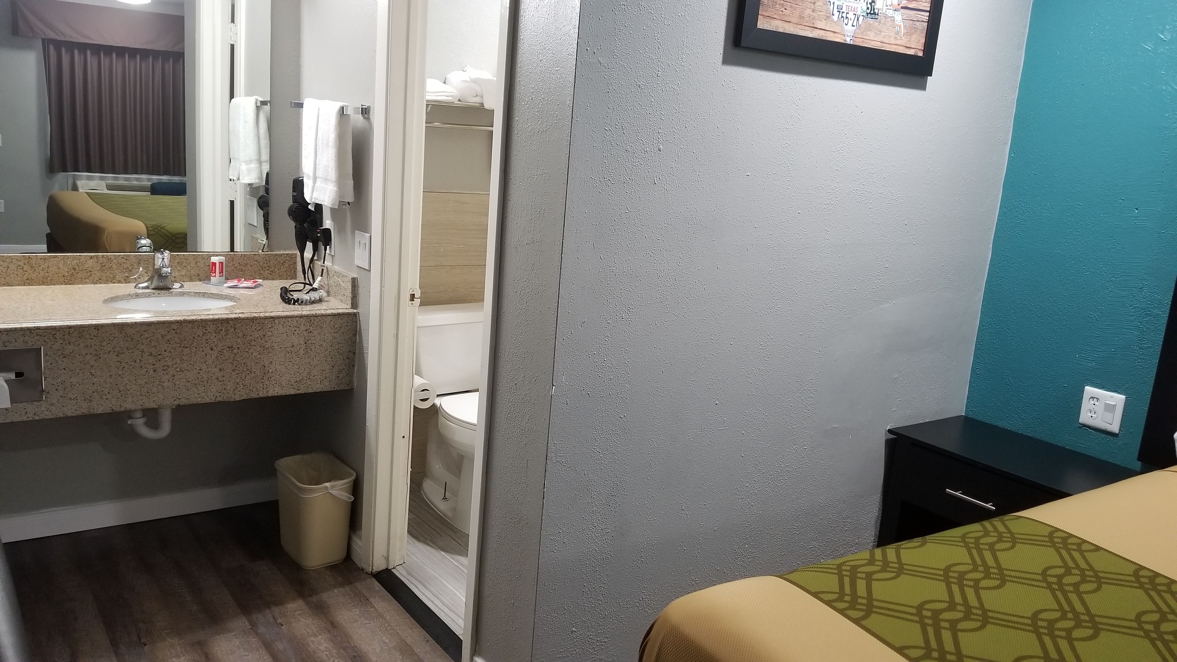 Habitación de hotel con baño, cama, cubo de basura y un cuadro colgado en la pared.