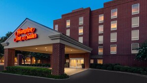 Un bâtiment de l’hôtel Hampton Inn & Suites, avec une façade en briques et un panneau lumineux au néon.