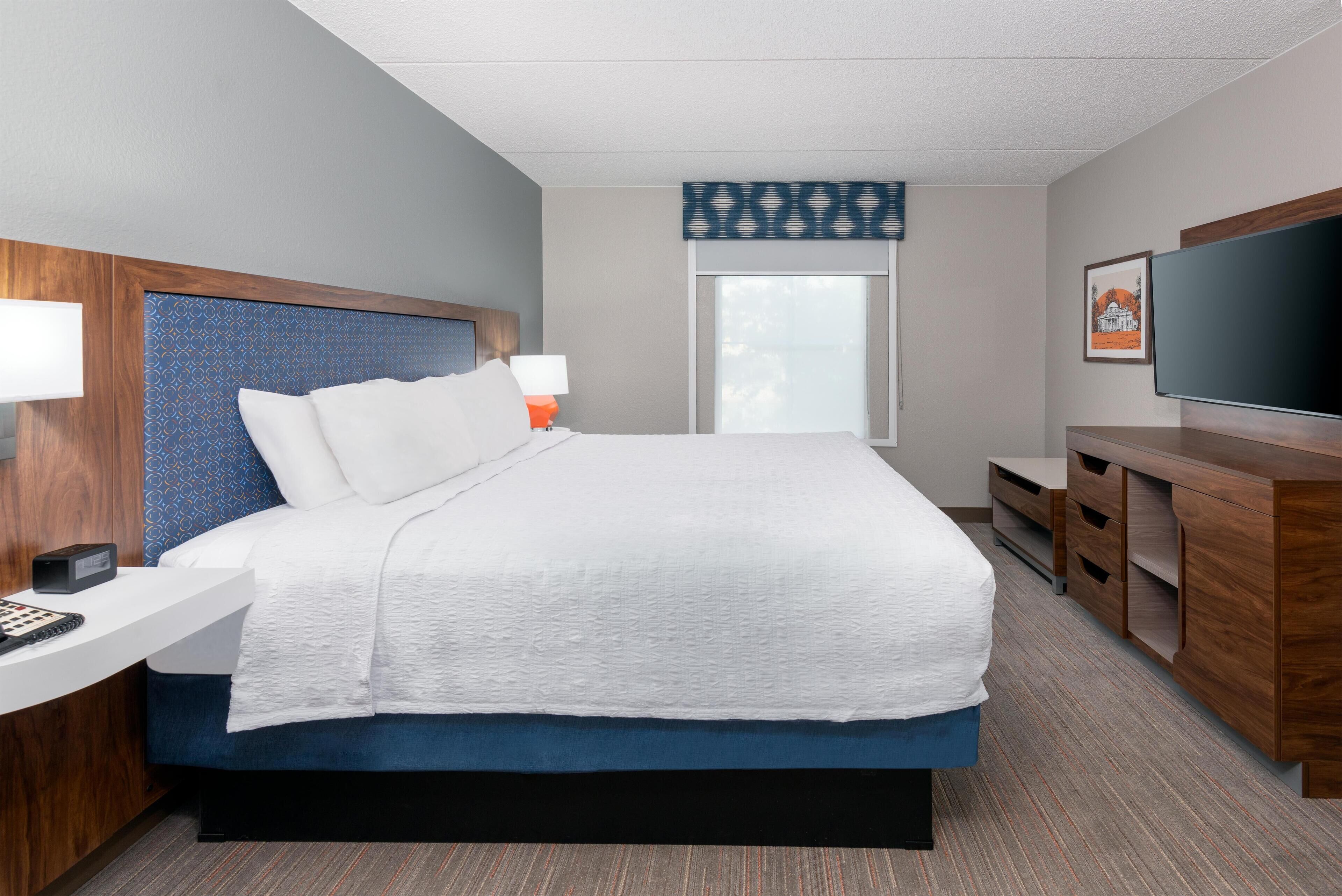 A hotel room with a bed, bedside table, TV, and a window with a view.