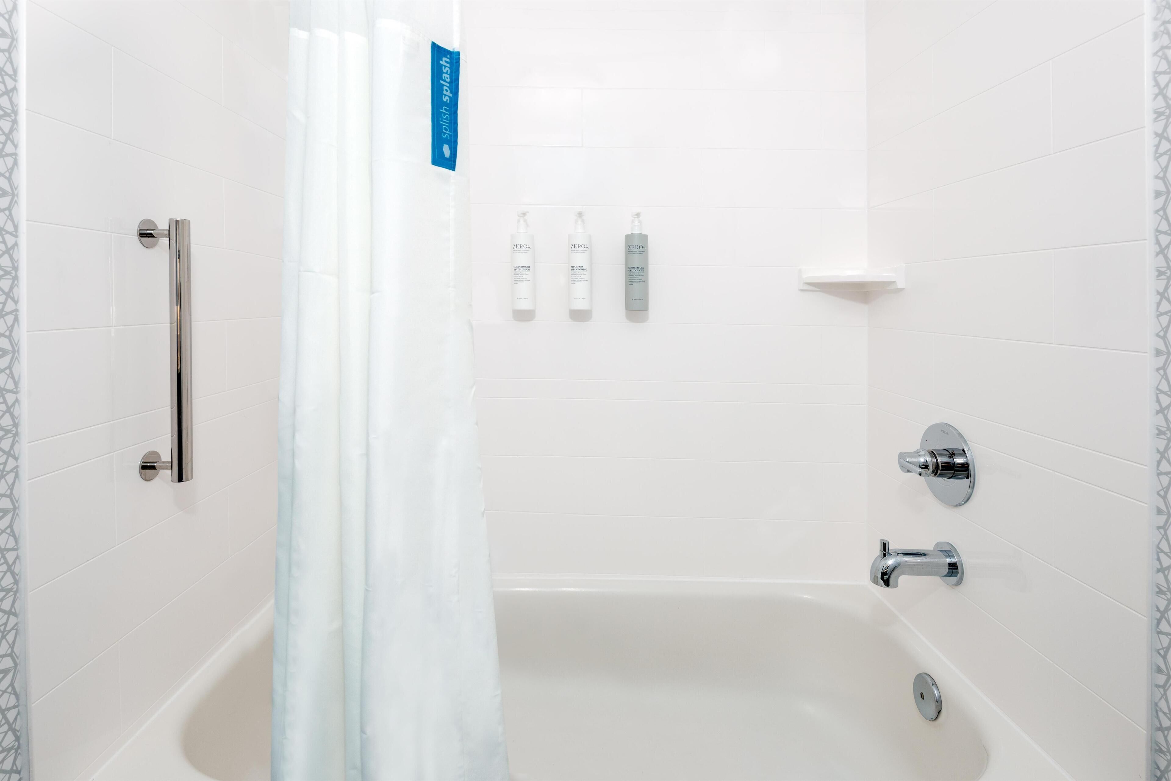 A modern bathroom with a bathtub, a handrail, and three bottles of shampoo on the wall.