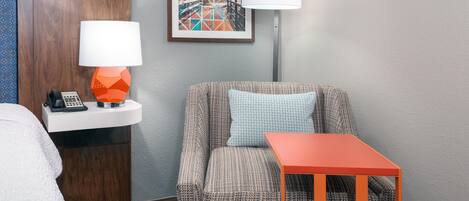 A hotel room with a bed, a small table with a lamp, a chair, and a wall-mounted phone.