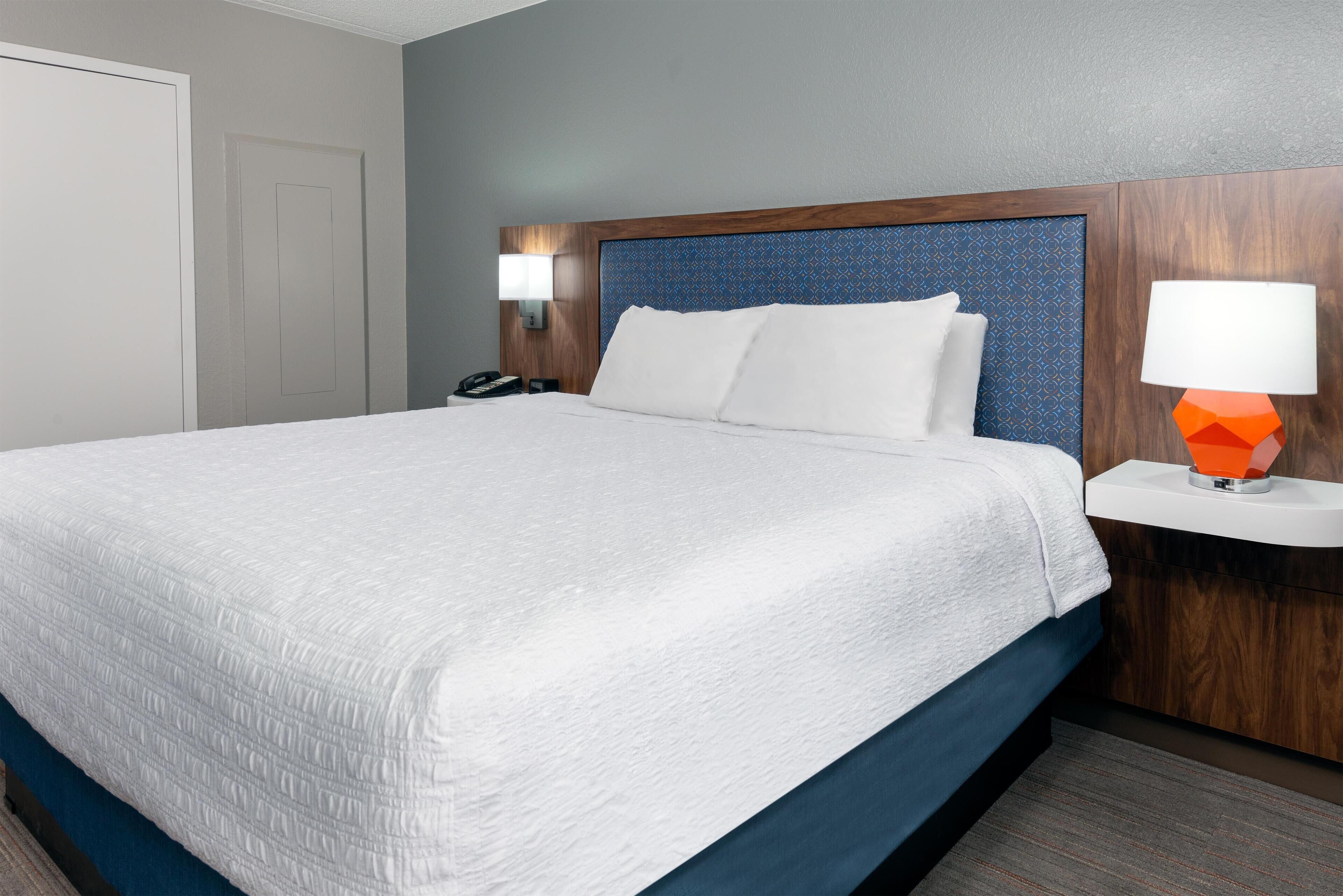 A hotel room with a large bed, a wooden headboard, a nightstand with a lamp, and a door.