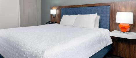 A hotel room with a large bed, a wooden headboard, a nightstand with a lamp, and a door.